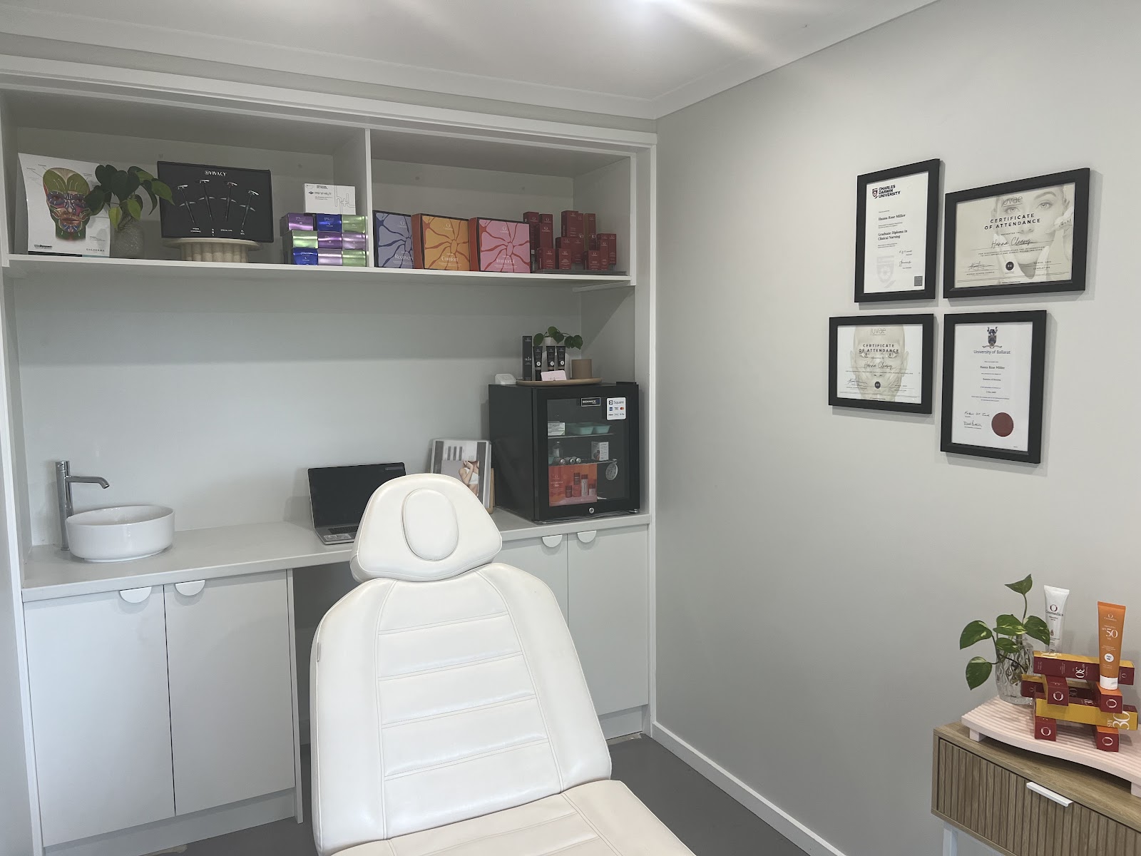 The Skin By Her treatment room, with a treatment bed, framed qualifications and shelves of skincare
